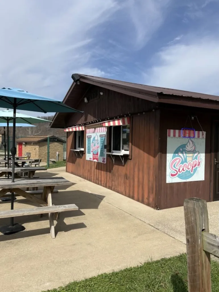 The Scoops stand in Barboursville Park: a brown wooden building with pink and white awnings over the windows, the Scoops sign, teal umbrellas and picnic tables