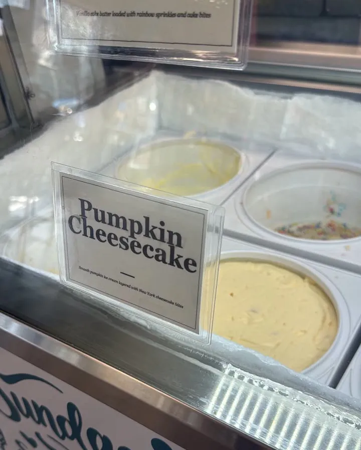 A tub of Pumpkin Cheesecake ice cream in the case with its paper placard