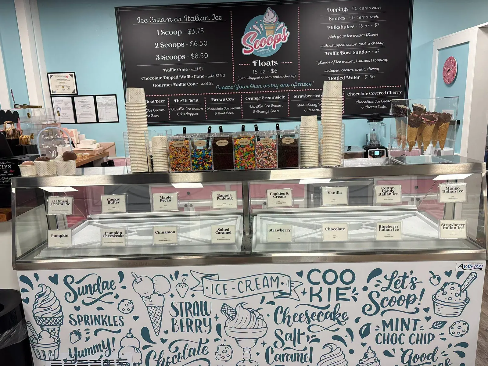The Scoops on Central counter: a chalkboard menu above a glass case of ice cream tubs, with aqua walls